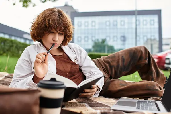 Curly-haired young woman balances freelance work while relaxing on a blanket in a park. — Stock Photo