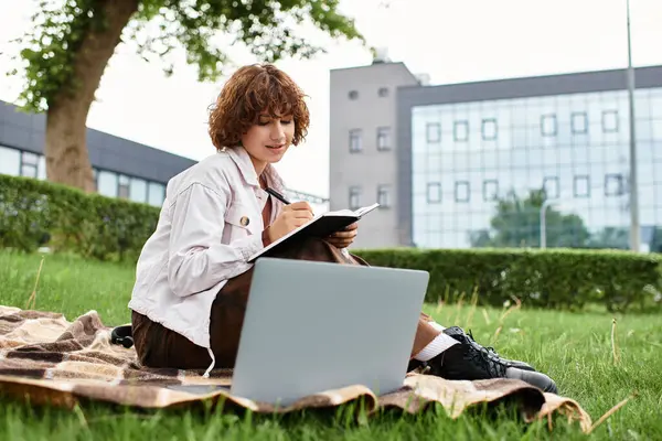 Young woman with curly hair works remotely on a blanket in a green park during summer days. — Stock Photo