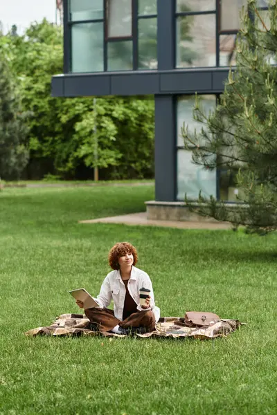 Curly-haired woman sits on a blanket, working remotely and sipping coffee on a sunny day. — Stock Photo