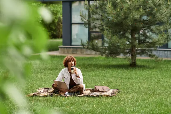 Young woman with curly hair works remotely on her laptop while enjoying coffee in a park. — Stock Photo