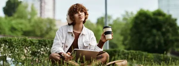 A young woman with curly hair relaxes on a blanket while sipping coffee in the park, banner — Stock Photo