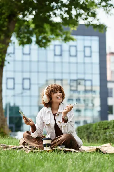 In a vibrant green park, a young woman sits happily on a blanket, immersed in her creative pursuits. — Stock Photo