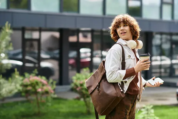 A young woman with curly hair relaxes outside her office, sipping coffee and checking her phone. — Stock Photo