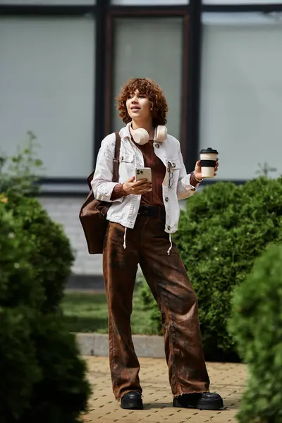 A young woman in casual clothing holds coffee while standing near her office building, smiling. — Stock Photo