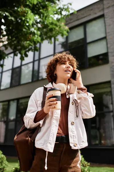 White jacket and headphones, she connects with someone while strolling near her modern workplace. — Stock Photo