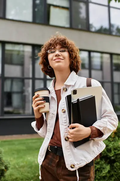A young woman with curly hair stands outside a sleek office building, sipping coffee. — Stock Photo