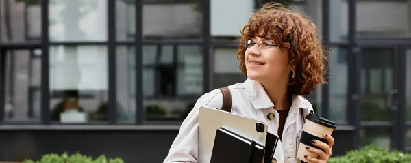 Curly-haired young woman in casual clothing smiles while holding a tablet and coffee, banner — Stock Photo