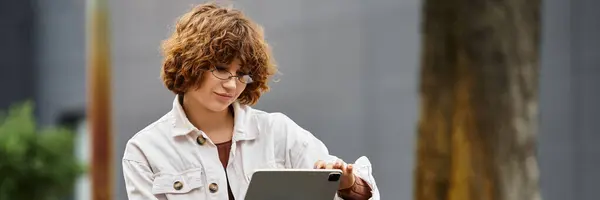 Curly-haired woman works peacefully outdoors on a tablet, surrounded by nature during summer days, banner — Stock Photo