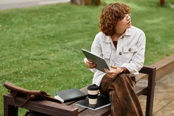 A curly-haired woman works remotely in a sunny park this summer. — Stock Photo