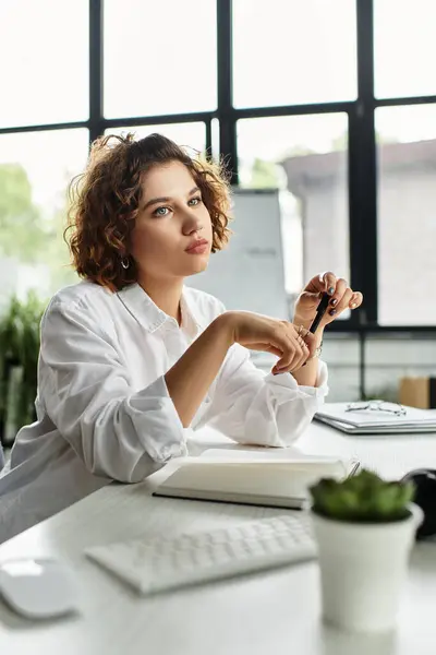 A young woman with curly hair ponders thoughtfully at her green-filled office workspace. — Stock Photo