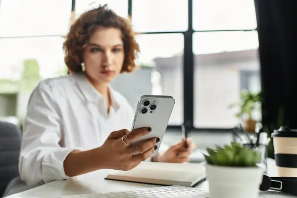 Curly-haired businesswoman focuses on her smartphone while working in a stylish office. — Stock Photo