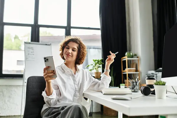 A young businesswoman with curly hair enjoys her smartphone while working in a stylish office. — Stock Photo