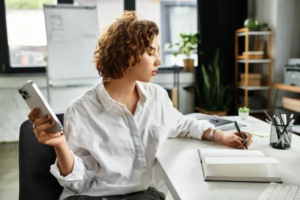 A young businesswoman writes notes while checking her phone in a stylish office setting. — Stock Photo