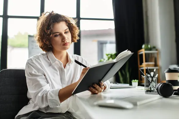 Curly-haired young businesswoman captures thoughts in a notebook while working at her desk. — Stock Photo