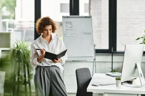Curly-haired businesswoman in smart casual attire engages with her notebook in a bright office. — Stock Photo
