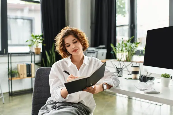 Curly-haired businesswoman writes in her notebook while working in a bright office. — Stock Photo
