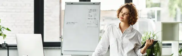 A young businesswoman with curly hair reviews notes while standing in a stylish office setting, banner — Stock Photo