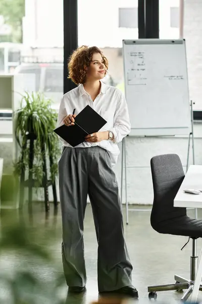 A young businesswoman with curly hair stands in a contemporary office, engaged in her work. — Stock Photo