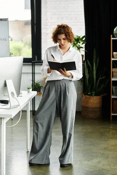 A professional woman with curly hair reviews notes while standing in her bright office space. — Stock Photo
