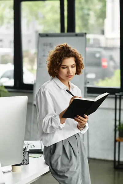 Young businesswoman with curly hair plans her tasks while standing in a contemporary office space — Stock Photo