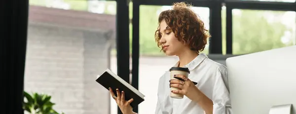 A young professional with curly hair reviews notes while holding coffee in a stylish office, banner — Stock Photo