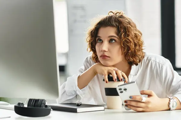 Focused young woman with curly hair thoughtfully handling coffee while working in the office. — Stock Photo