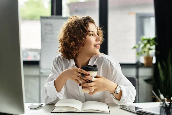 A young woman with curly hair sips coffee and thinks creatively in her smart casual office. — Stock Photo