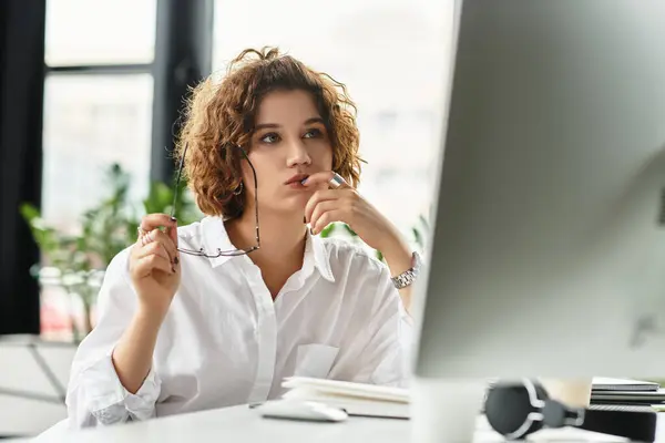 Curly-haired young woman engages in serious work at her office desk during summer. — Stock Photo