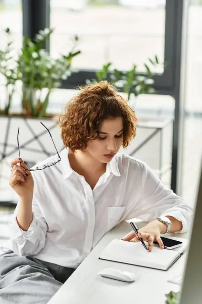 Curly-haired businesswoman in smart casual attire takes notes while evaluating plans during summer. — Stock Photo