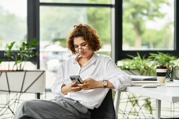 Businesswoman with curly hair uses her phone while seated in a stylish office setting. — Stock Photo