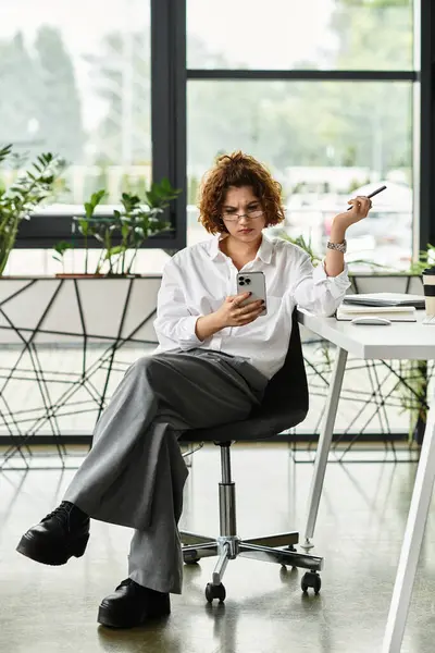 A young professional with curly hair multitasks on her phone in a lively office. — Stock Photo