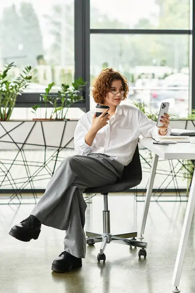 A young businesswoman with curly hair engages with her phone while seated in a stylish office space. — Stock Photo