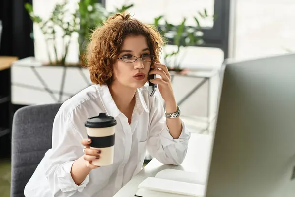 A young businesswoman with curly hair talks on her phone while holding a coffee cup, focused. — Stock Photo