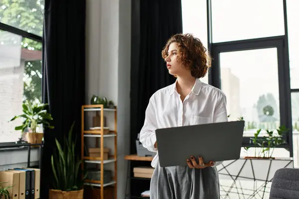 A young woman in smart casual attire focuses on her laptop while standing in a contemporary office. — Stock Photo
