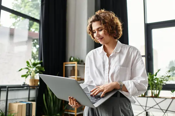 A young businesswoman with curly hair engages with her laptop in a stylish office environment. — Stock Photo