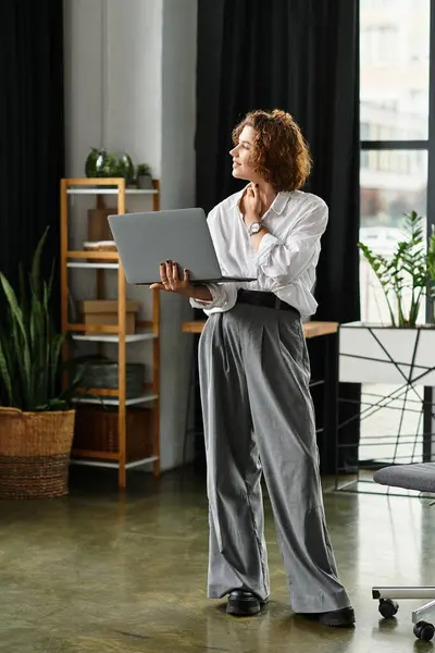 A young professional with curly hair brainstorms while holding a laptop in a modern office. — Stock Photo
