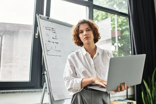 A young businesswoman with curly hair engages with her laptop while analyzing data charts. — Stock Photo