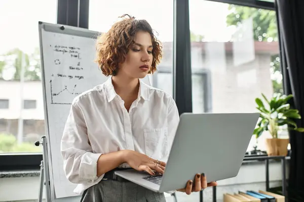 Young professional with curly hair focuses on her laptop in a bright, stylish office space. — Stock Photo