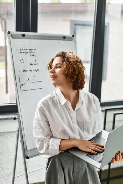 Curly-haired young professional collaborates in a bright office space with charts nearby. — Stock Photo
