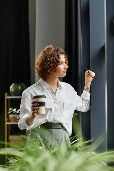Curly haired young businesswoman gazes thoughtfully out the window while holding coffee. — Stock Photo