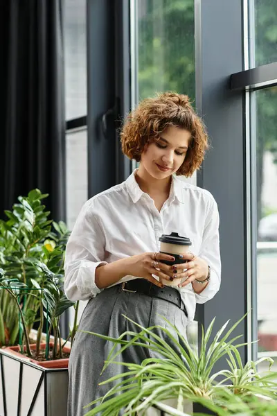 Curly-haired businesswoman in smart casual attire relaxes with a coffee in the office. — Stock Photo