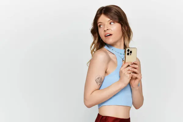 A young woman shows summer vibes in a trendy top, playfully holding her smartphone. — Stock Photo