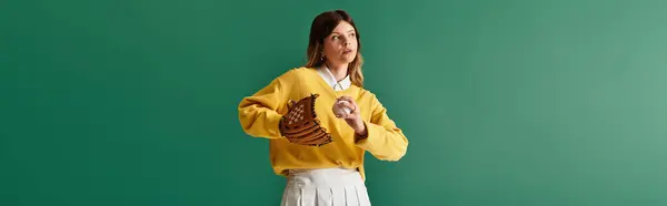 A confident young woman prepares to throw a baseball against a bright backdrop. — Stock Photo