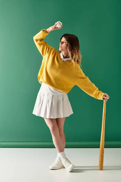 A cheerful young woman in a yellow sweater and white skirt prepares to throw a ball. — Stock Photo
