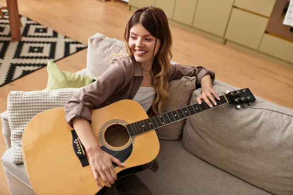 A cheerful young woman relaxes on her couch, playing guitar and soaking up the summer atmosphere. — Stock Photo