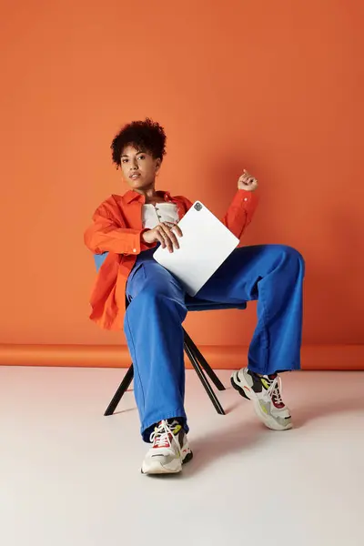 Eine stilvolle Frau mit lockigem Haar interagiert mit ihrem Gerät in einem lebendigen, farbenreichen Studioraum. — Stockfoto