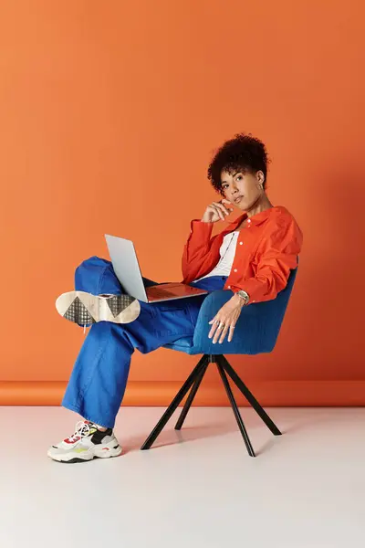 Кучерява жінка, одягнена в модний одяг, взаємодіє зі своїм ноутбуком у яскравій обстановці. — Stock Photo