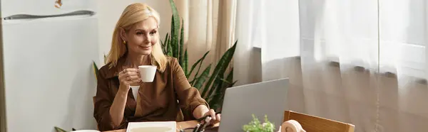 Elegant senior woman sips coffee at her desk, surrounded by lush plants and warm sunlight. — Stock Photo
