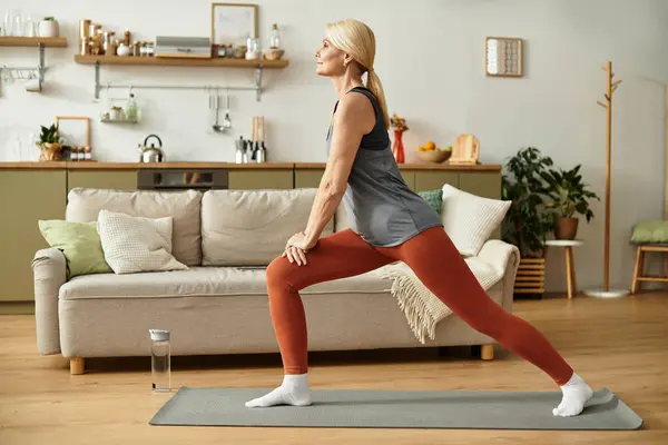 Una hermosa mujer mayor realiza posturas de yoga en un espacio vital luminoso y acogedor. - foto de stock