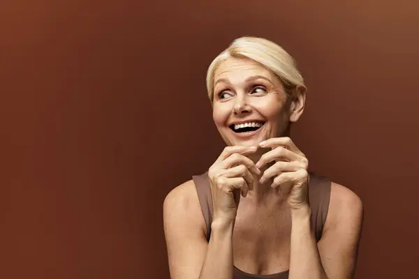 Con una sonrisa radiante, una elegante mujer mayor mira juguetonamente hacia la cámara, exudando felicidad. - foto de stock